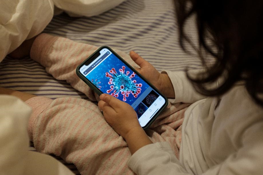 A two-year-old looks on a phone at an illustration of a microscopic view of the new coronavirus. Picture: Marzio Toniolo/Reuters