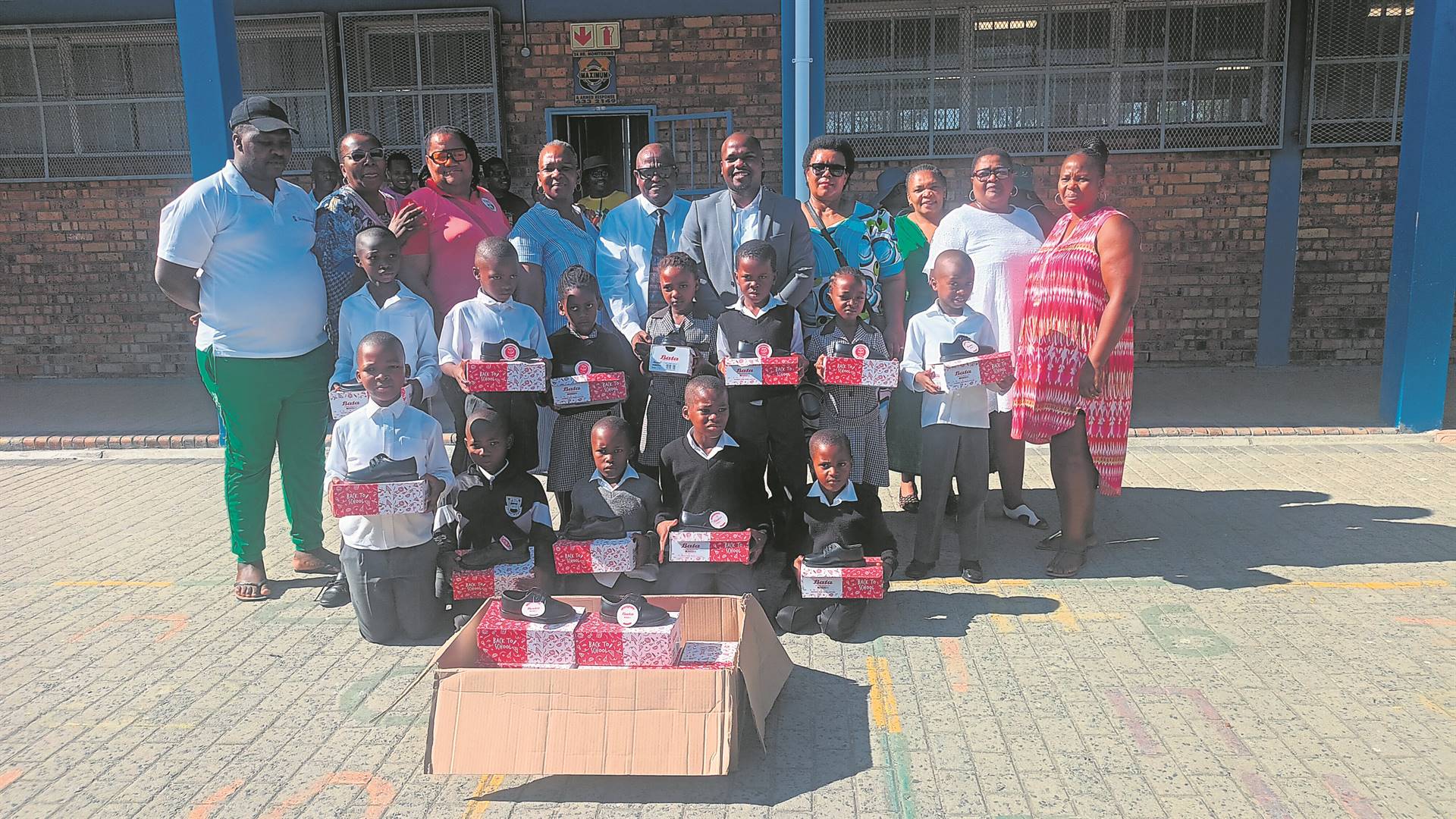 Mokone learners show off their new shoes as staff members together with ward councillor Lwazi Phakade (wearing grey suit) and parents behind them look on. PHOTO: Unathi Obose