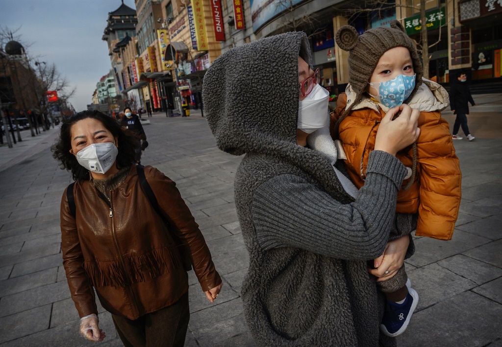 A woman and her child wear protective masks a nearly empty commercial street in Beijing on 18 February. (Photo by Kevin Frayer)