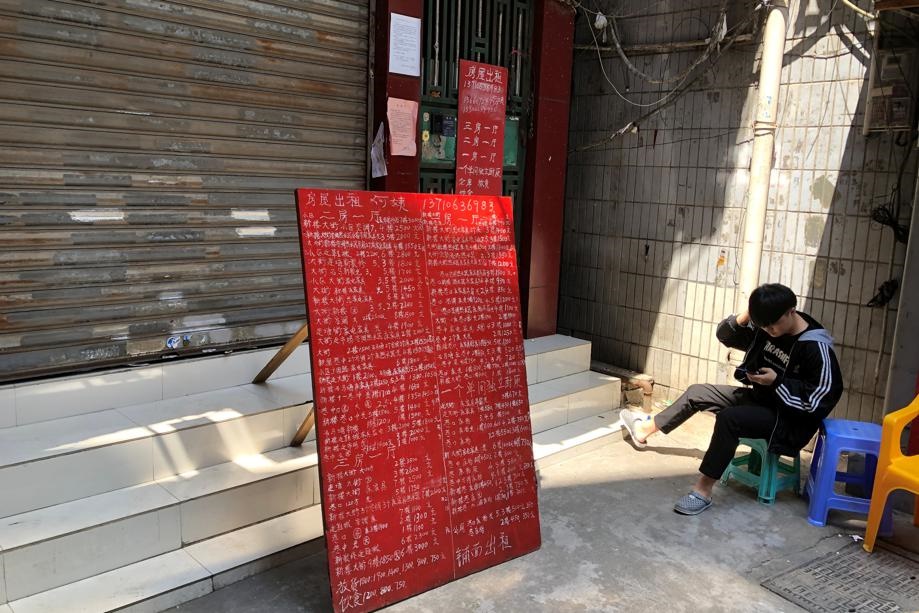 A resident checks his phone next to a sign advertising apartments in the area around Sanyuanli's trading hub in Guangzhou, following an outbreak of the Covid-19 coronavirus, Guangdong province, China. Picture: David Kirton/Reuters