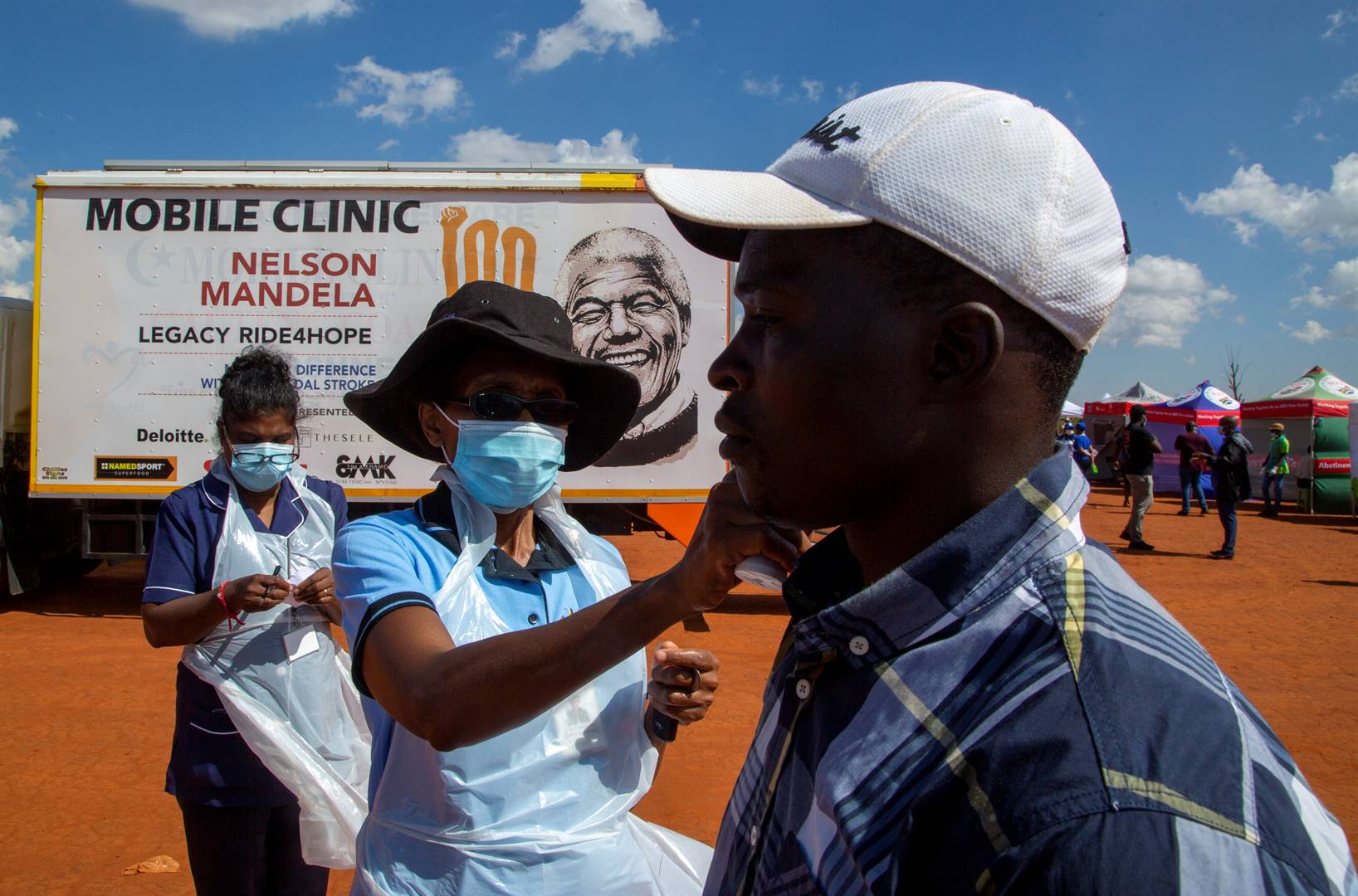 A health worker checks the temperature of a man queueing on a soccer field to be screened and tested for Covid-19 in Lenasia South, Johannesburg. Picture: Themba Hadebe/AP Photo