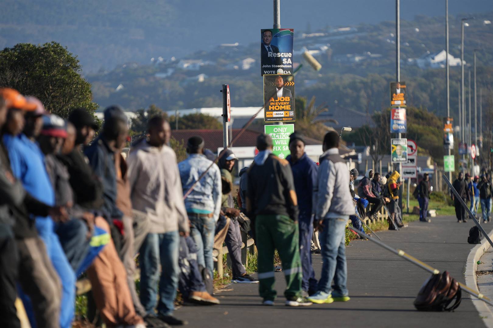 Werksoekers in Kaapstad staan by lamppale bedek met verkiesingsplakkate.  Foto: Reuters