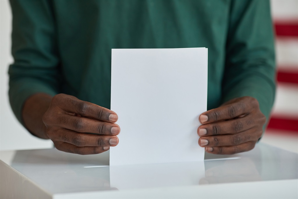 Close-up of Afro-American voter holding ballot standing near the ballot box