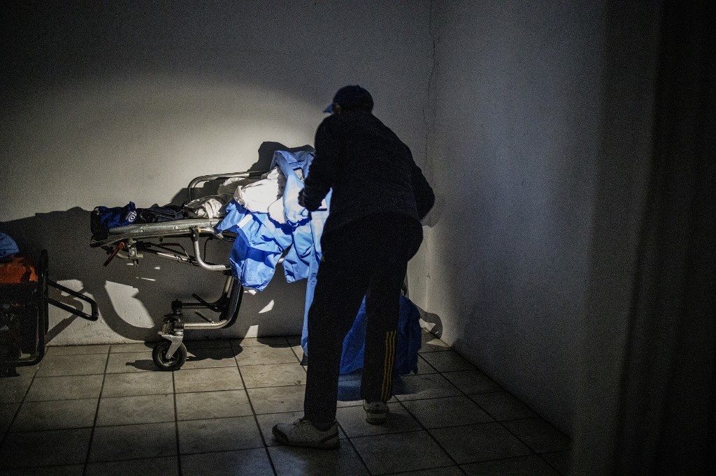 Sello Headbush, the owner of a funeral parlour, uses the light from his mobile phone during load shedding to check on a heap of discarded PPE left on a stretcher in front of the cold storage room in Port Elizabeth.