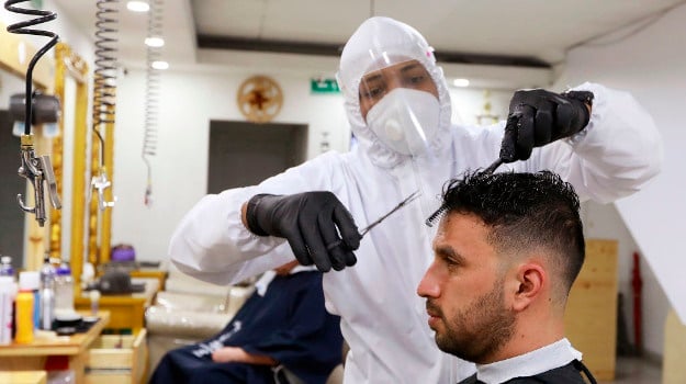 A hairdresser wearing a protective suit, gloves and a face mask gives a man a haircut in a barbershop amid the Coronavirus pandemic on in Bogota, Colombia. (Photo by John Vizcaino/VIEWpress via Getty Images)