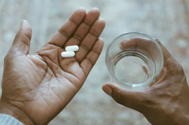 woman holding pills and a glass of water (PHOTO:GETTY IMAGES)