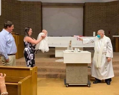 a priest baptising an infant with a water gun