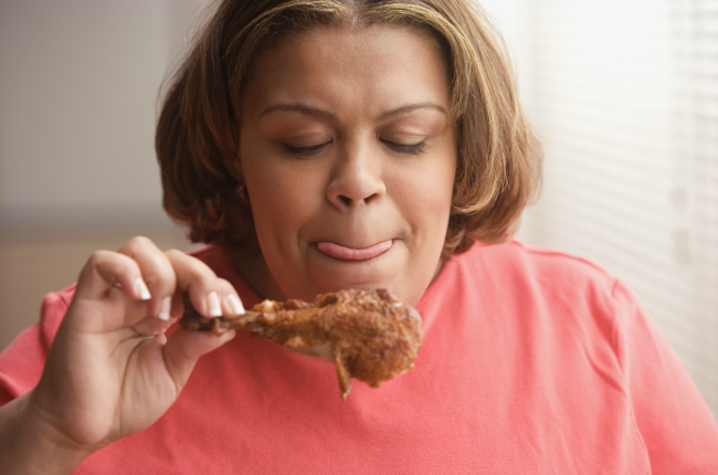  Woman licking her lips and looking at a piece of fried chicken.