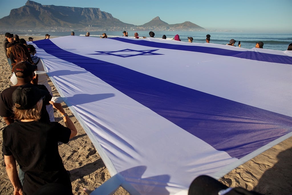 A giant Israeli flag held by Jews and Christians in support of Israel at Lagoon Beach in Cape Town on 16 December 2023. (Stringer/AFP)