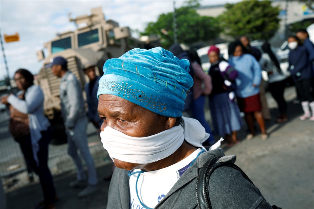 An elderly woman covers her face with a makeshift mask as people queue to collect social grants in Khayelitsha township near Cape Town. 