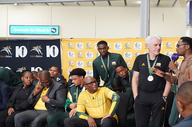 Bafana Bafana coach Hugo Broos being engaged with SABC Sports presenter Andile Ncube at their rapturous welcome at the OR Tambo Airport while Ronwen Williams looks on. (Image: Alfonso Nqunjana/News24)