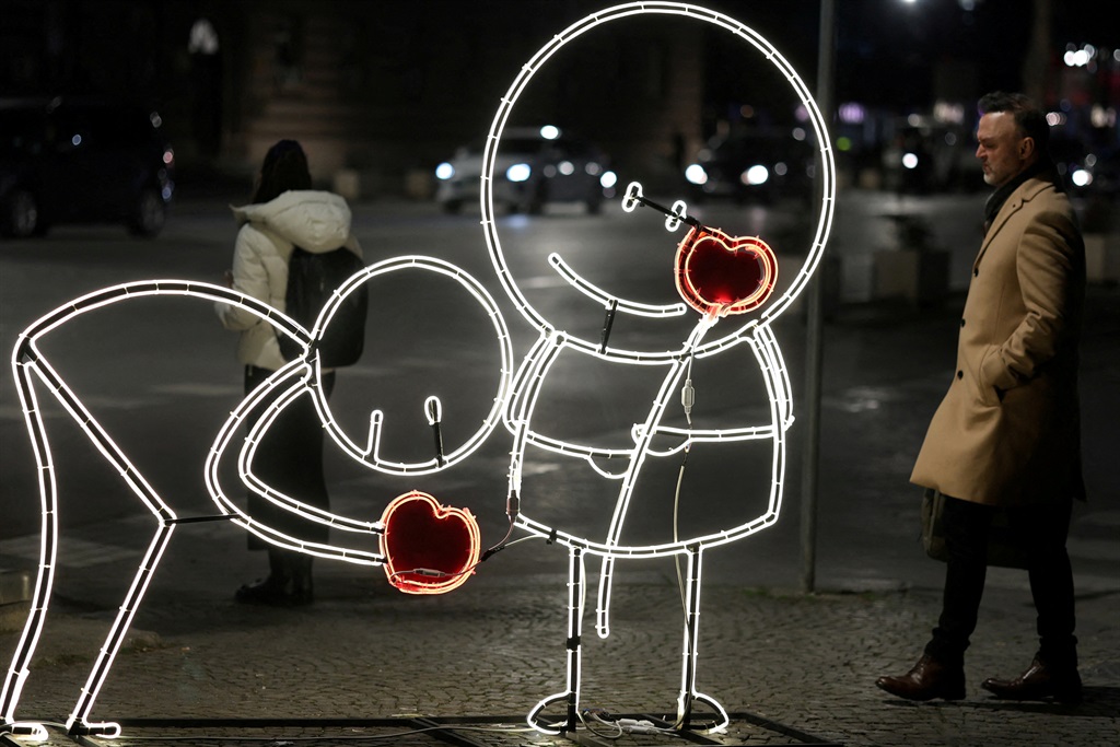 People pass by a light decoration during Valentine
