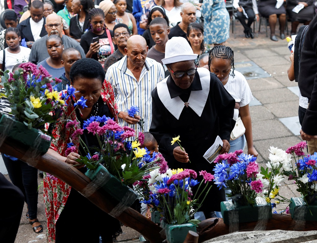 People place flowers on a cross during a silent Go