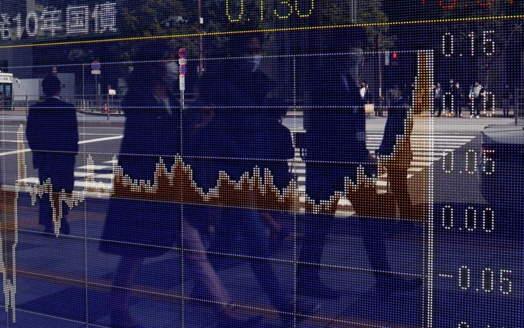 Pedestrians are reflected on an electric board showing stock prices at a business district. 