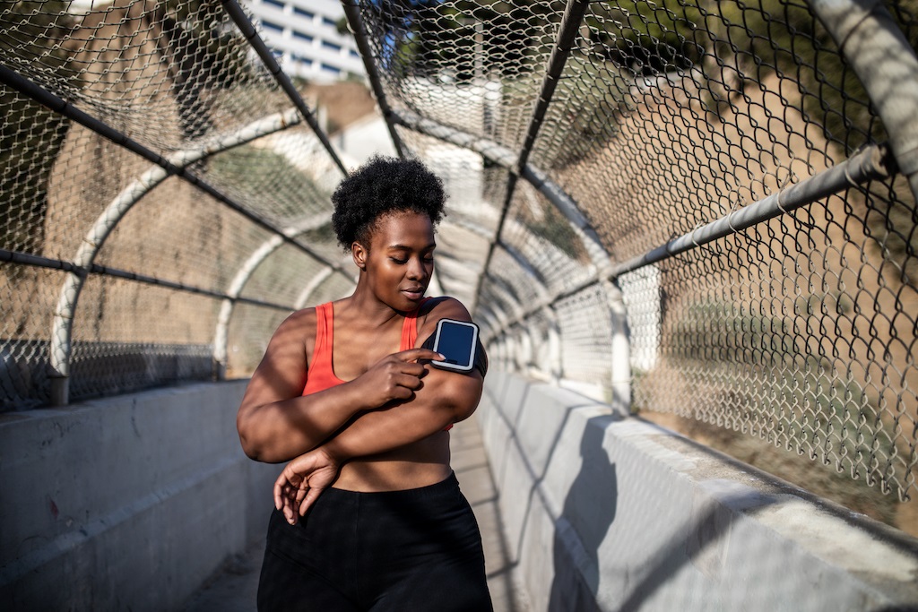 Healthy woman touching phone screen on armband before exercising outdoors. 