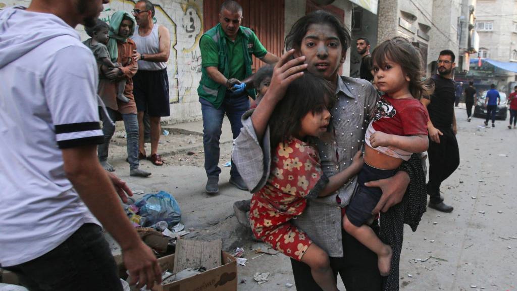 A Palestinian girl holds two children as she stands on a street in Gaza City on 12 October 2023 as raging battles between Israel and the Hamas movement continue.