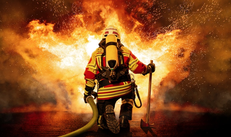 Ein Feuerwehrmann steht vor einer groÃ?en Aufgabe. Er ist mit schwerem Atemschutz ausgerÃ¼stet und trÃ¤gt eine SchutzausrÃ¼stung, die ihn vor der Hitze und den Flammen schÃ¼tzt.