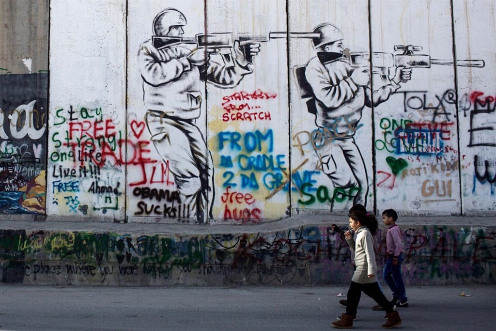 Children walk past graffiti on the Palestinian side of the separation wall in Bethlehem, West Bank. (Photograph by Chris McGrath/Getty Images)