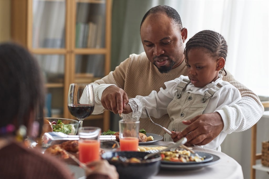 Stock photo: Dad sitting at table with child, helping her eat her meal during family dinner.