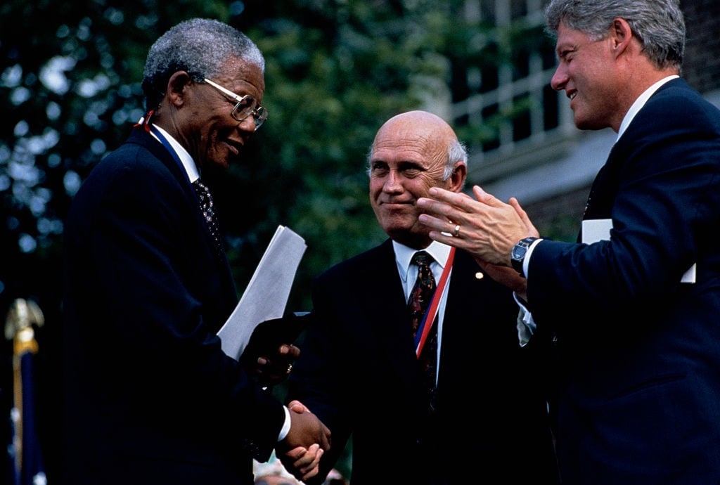 President Clinton applauds as Nelson Mandela, South Africa's first post-Apartheid President, and Frederik de Klerk, South Africa's last Apartheid President, shake hands. Both Mandela and de Klerk won the Nobel Prize for peace.