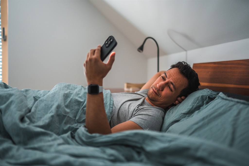 Man scrolling through his phone while laying in bed alone. 