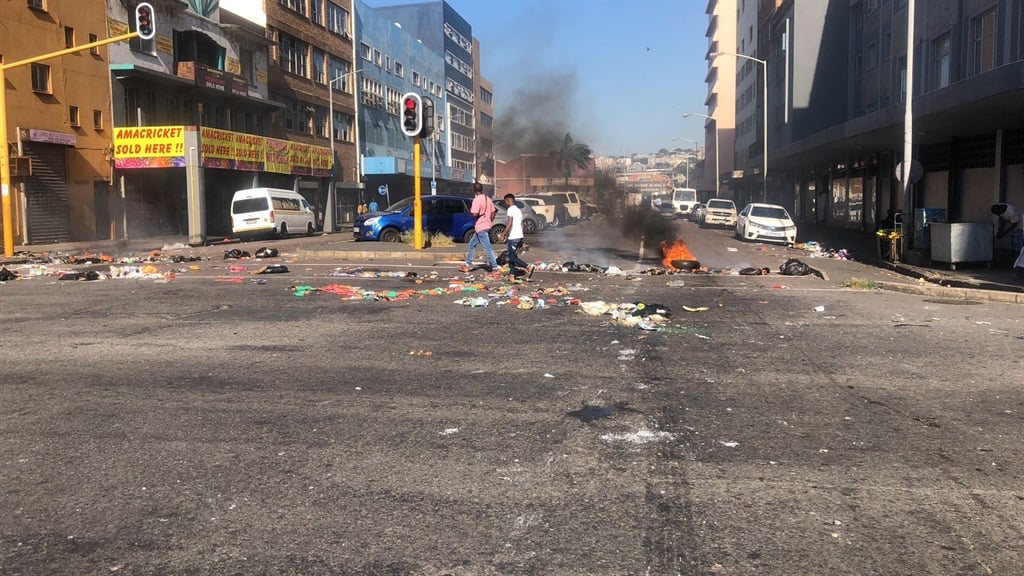 Two people walk past a burning tyre in the Durban CBD. 