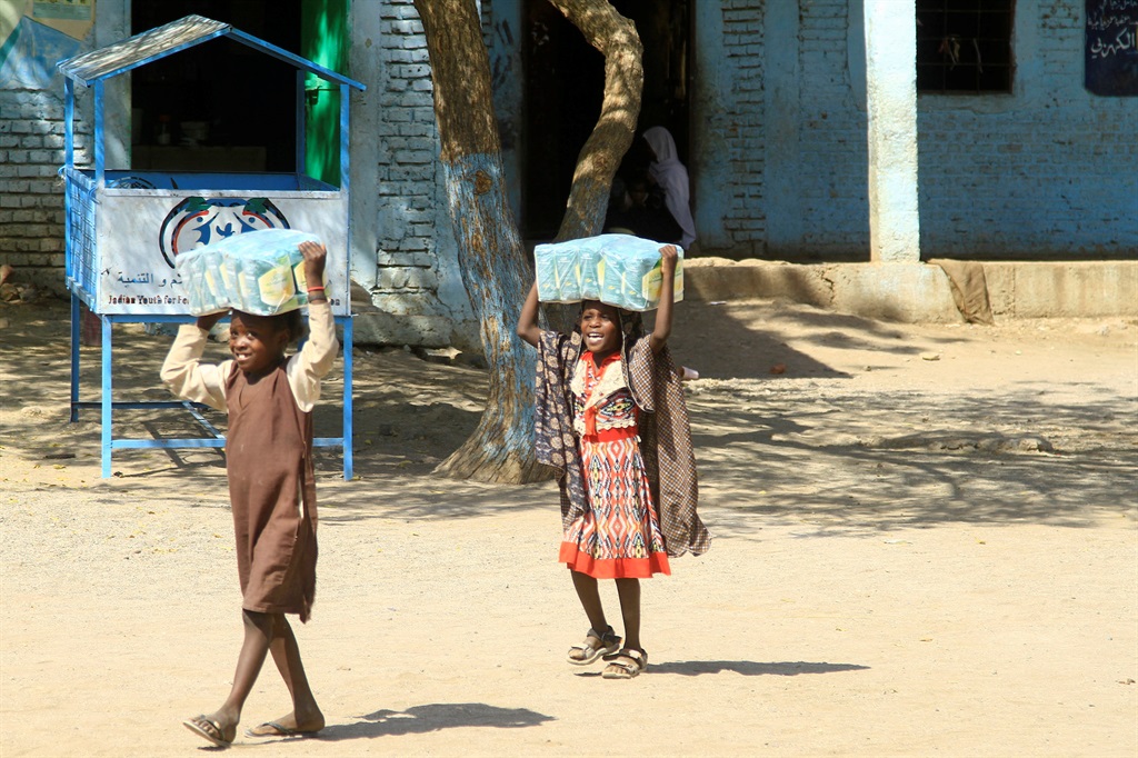 Displaced Sudanese children carry packs of humanit