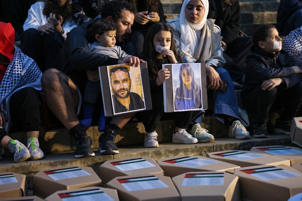Demonstrators display portraits of Reuters journalist Issam Abdallah (L) and Al-Mayadeen TV reporter Farah Omar, killed in separate instances while covering the frequent exchanges of fire across Lebanons border with Israel, while sitting in front of symbolic coffins in Beirut on 8 December 2023. (Joseph EID / AFP)