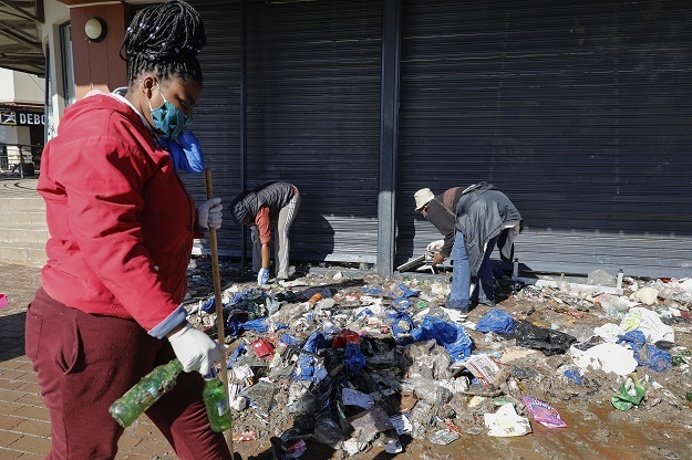 A woman holds empty beer bottles outside a liquor store as others sort rubble while volunteering to clean the Diepkloof Square on Wednesday. 