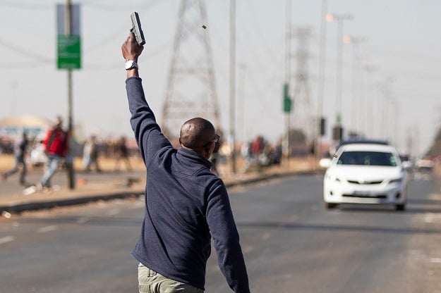 A man fires a hand gun in the air to disperse a mob of alleged looters outside of the Chris Hani Mall in Vosloorus. Photo: Guillem Sartorio/AFP