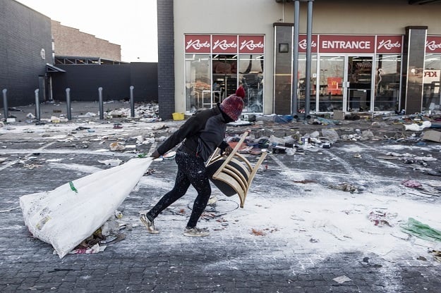 A suspected looter pulls a few items along the ground outside a vandalised mall in Vosloorus. 