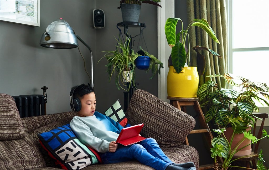 Child sitting on sofa at home, concentrating on device.