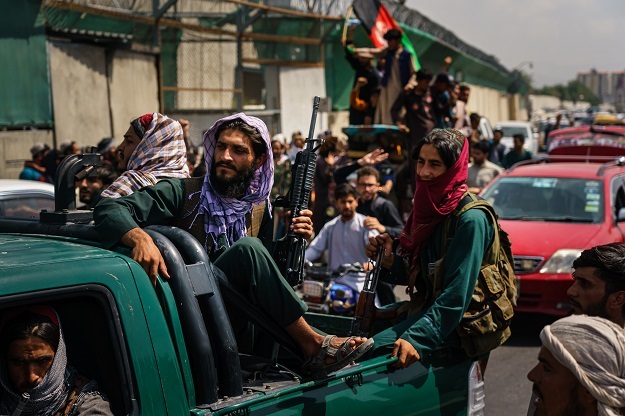 Afghans march down the street carrying banners and the flag of the Islamic Republic of Afghanistan, despite the presence of Taliban fighters around them.