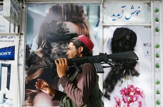 A Taliban fighter walks past a beauty salon with images of women that have been defaced in the Afghan capital, Kabul. As the ultra-conservative Islamic group regains power, there’s great concern for what life is going to be like for the country’s women. (PHOTO: Gallo Images/Getty Images)