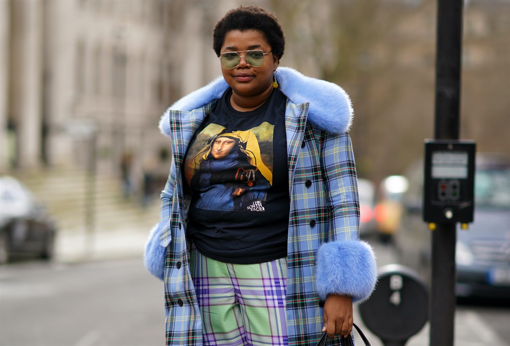 Gabriella Karefa-Johnson wears glasses, a blue checked coat with fluffy cuffs and collar, a pink bag, cropped pants, white pointy shoes, a t-shirt with a printed picture depicting Mona Lisa, during London Fashion Week February 2020 on February 17, 2020 in London, England. (Photo by Edward Berthelot/Getty Images)