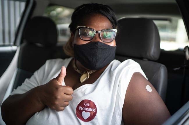 Portrait of a happy woman in a car with a get vaccinated sticker - wearing face mask