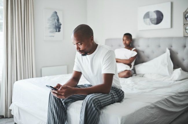 Picture of a young man ignoring his wife while using a smartphone in the bedroom at home.
PeopleImages / getty images