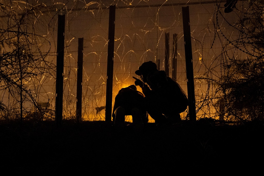 Men watch for US authorities while shearing an opening through a razor wire-laden fence for a group of migrants from South and Central America to enter into the United States from along the bank of the Rio Grande River, in El Paso, Texas, on 2 April 2024.    