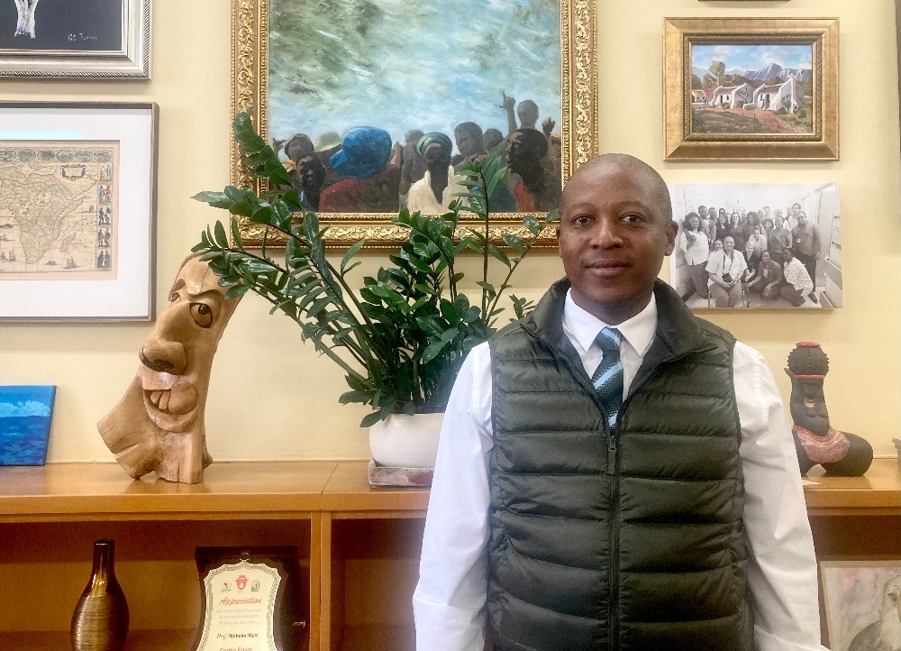 Professor Ntobeko Ntusi in front of a painting depicting student protests inside his office at Groote Schuur Hospital - the same office that once housed his mentor, the late Professor Bongani Mayosi. (Biénne Huisman/Spotlight)