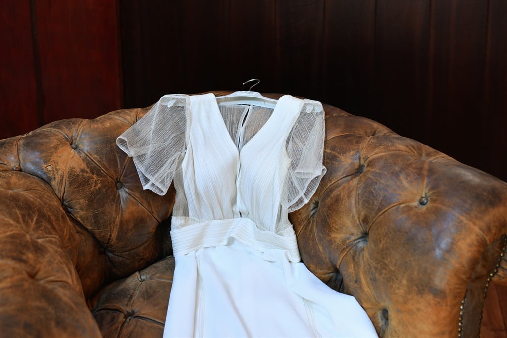 Wedding dress lies on a vintage brown leather chair.
