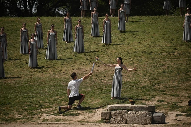 Greek actress Mary Mina (R), playing the role of the High Priestess, lights a Paris 2024 Olympics torch held by first torch bearer, Greek rowing Olympic champion Stefanos Ntouskos at the ancient temple of Hera on the Olympia archeological site, birthplace of the ancient Olympics in southern Greece, on 15 April 2024.(ANGELOS TZORTZINIS/AFP)