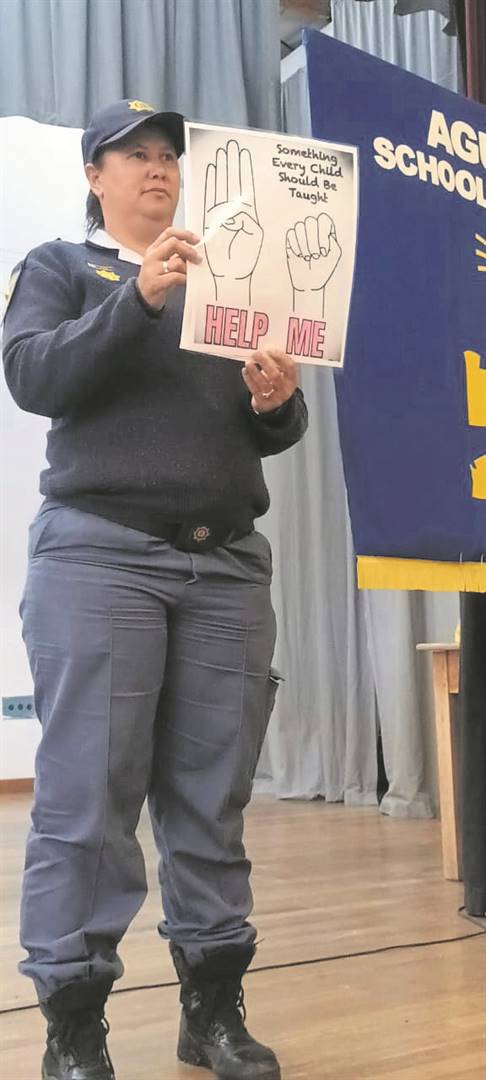 Sergeant Lorianne Dyers of Napier police with a poster showing the learners of the Agulhas School of Skills how to signal for help using their hands. 