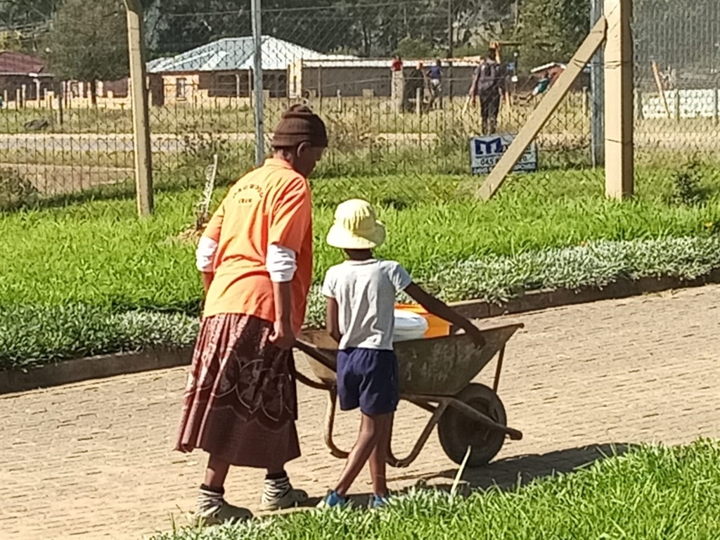 Nomantombi Ngabaza (69) pushes her wheelbarrow after filling her containers while her grandson watches on.
