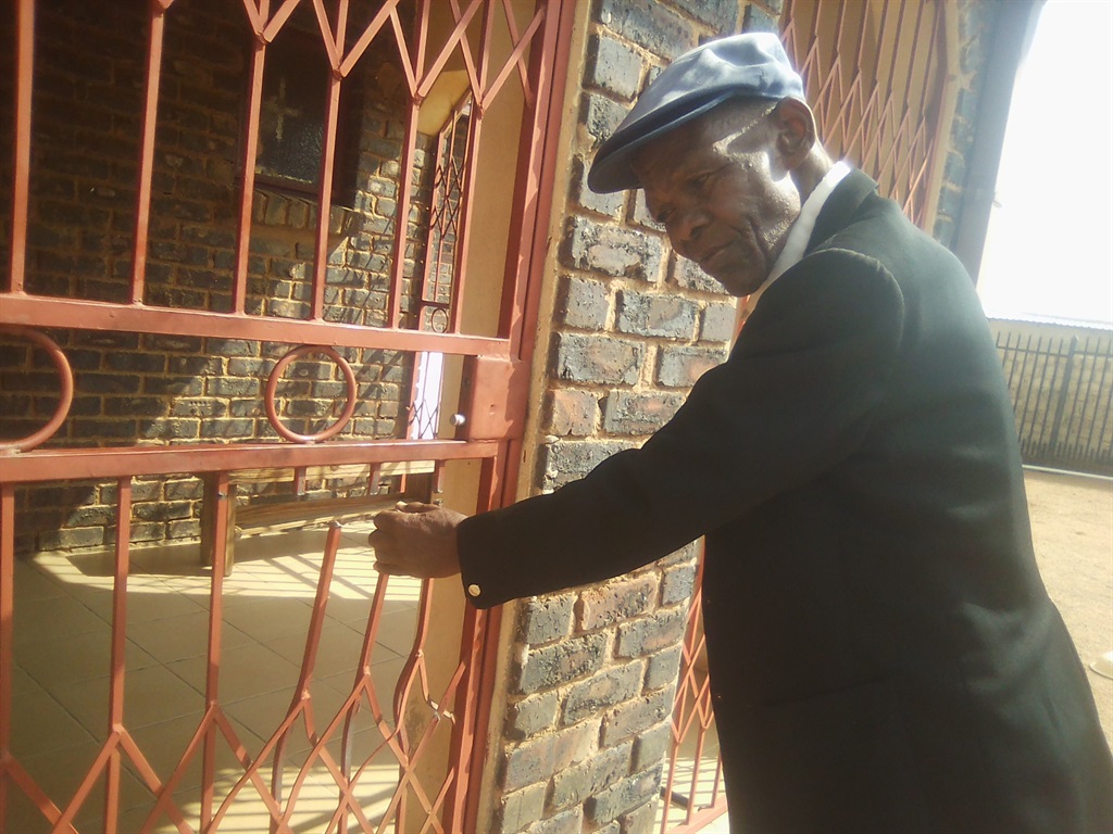 John Mashilo points out the damaged security gate that the thugs broke through. Photo by Bongani Mthimunye