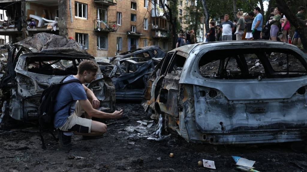 A young man examines his car destroyed by a missil