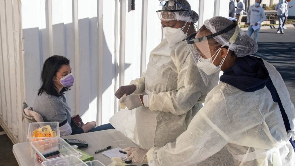 Health workers wearing personal protective equipment (PPE) prepare to test a woman for Covid-19. (Emmanuel Croset/AFP)