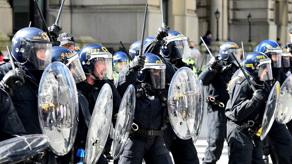 Police officers in riot gear gesture with batons d