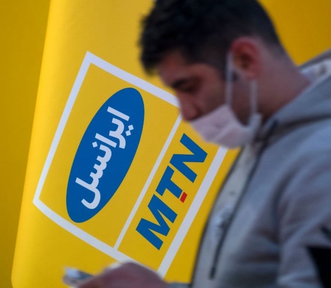 An Iranian man uses his smartphone as he walks past a MTN-Irancell logo in Tehran. (Morteza Nikoubazl/NurPhoto via Getty Images)