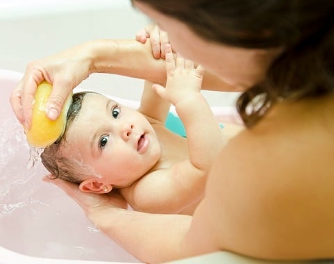 mother cleaning little baby in bathtub with sponge
