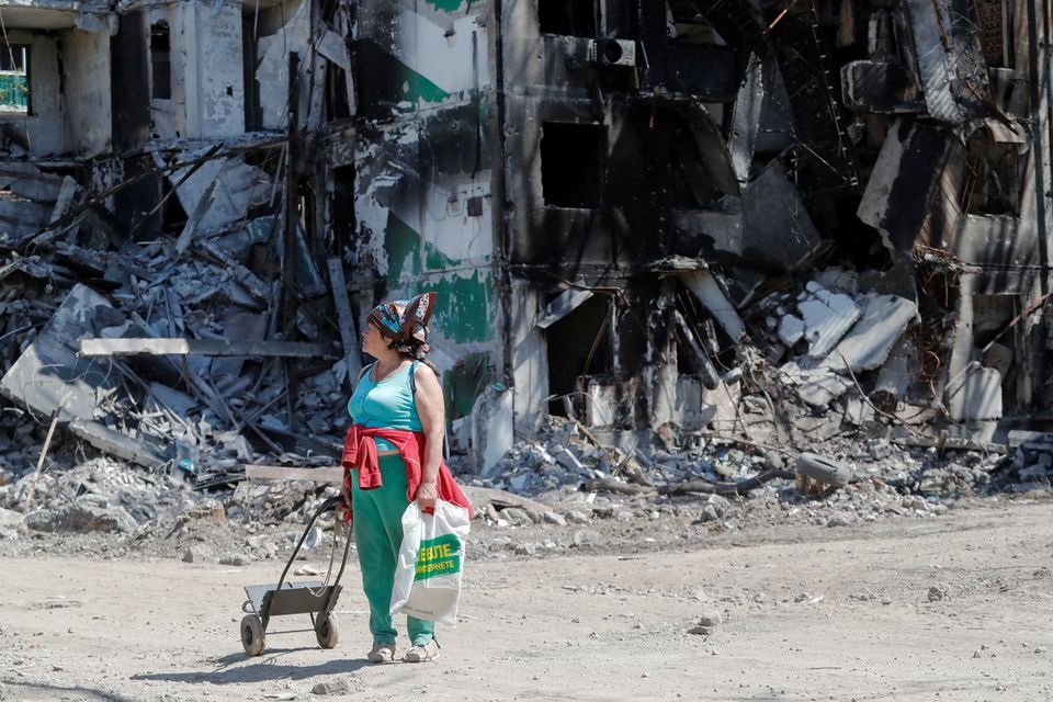 'n Vrou staan naby 'n vernietigde residensiële gebou in die suidelike hawestad van Marioepol in Oekraïne. Foto: REUTERS/Alexander Ermochenko